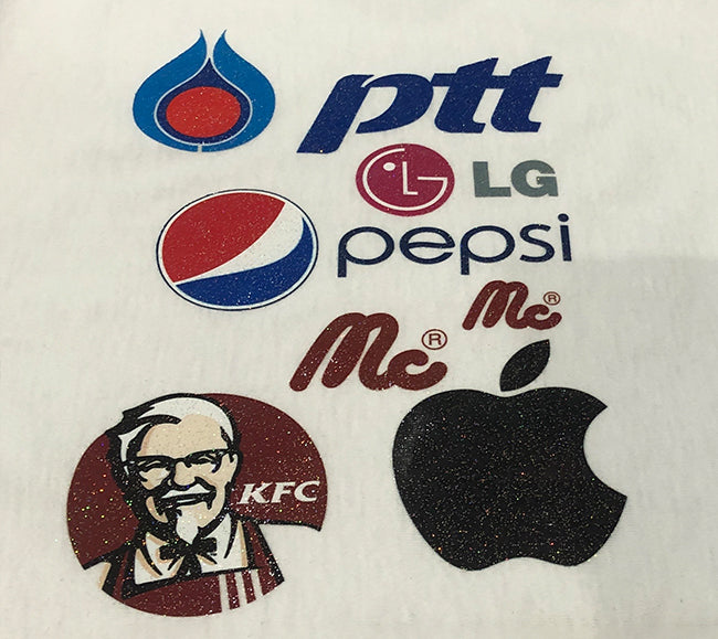 Close-up of glitter DTF transfers on white fabric showing logos with a fine sparkle finish